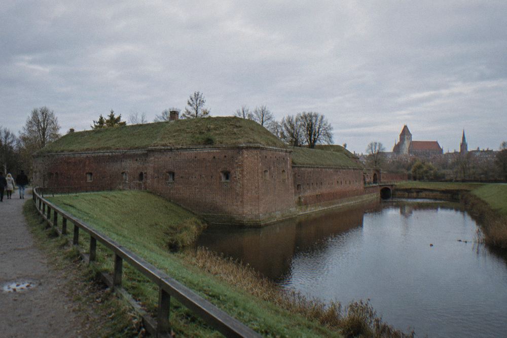 An earthen rampart and moat surrounding an old brick fort under a wide sky