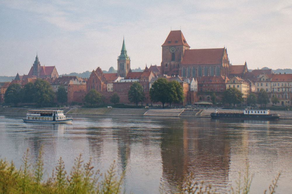 Panorama of Toruń Old Town seen from across the Vistula river, with red brick gothic buildings and church towers under a daytime sky