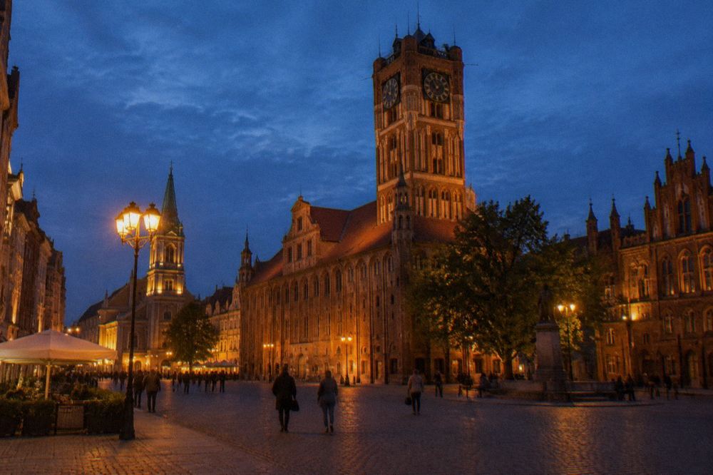 Evening view of Toruń Old Town Hall tower and market square with lit gothic facades