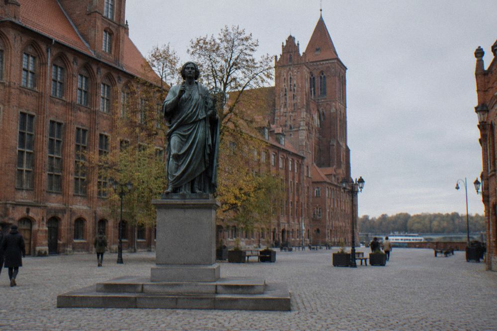 The bronze statue of Copernicus standing on Rynek Staromiejski in Toruń, with Gothic townhouses behind it