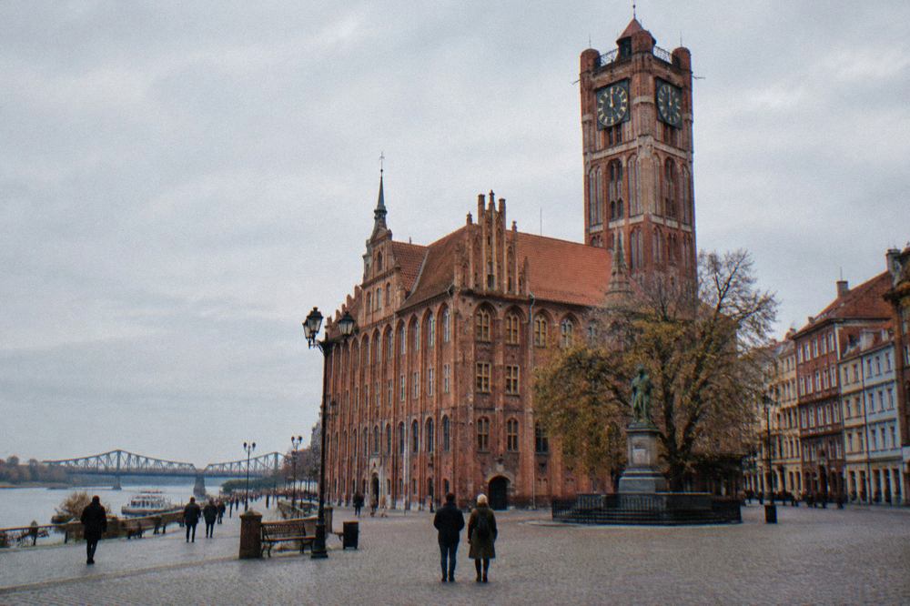 Gothic brick townhouses and a tower rising over a cobbled square in the Old Town of Toruń