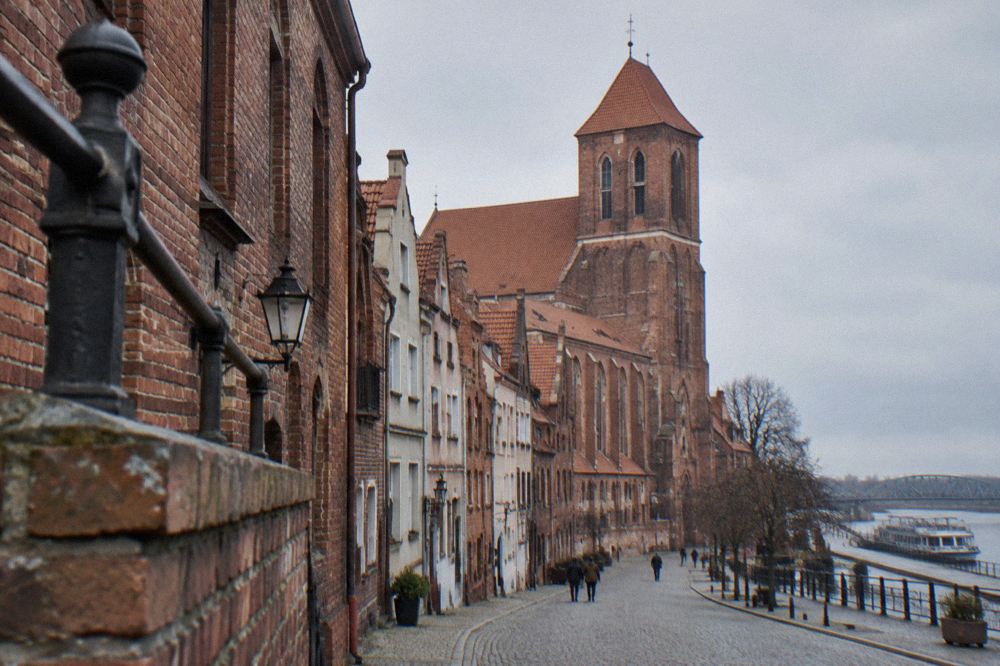 Red-brick gothic church and townhouse facades along a cobbled street in Toruń's old town