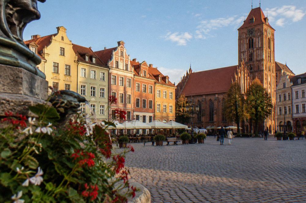 Cobbled market square in the Toruń New Town with colourful townhouses under a blue sky