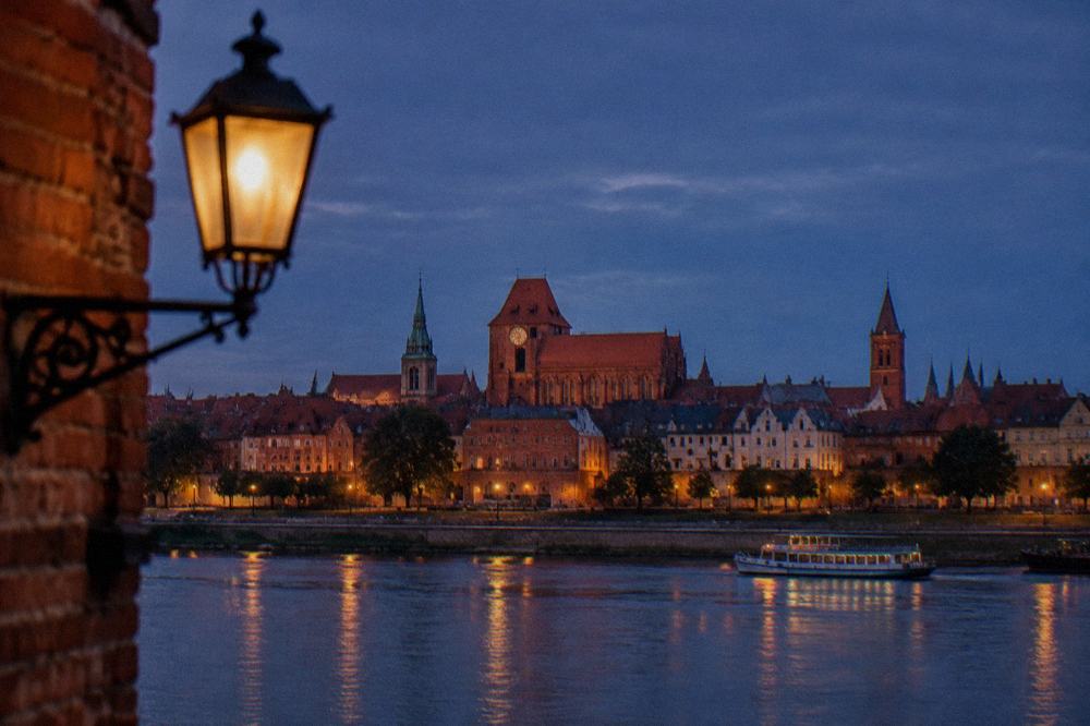 Evening view over Toruń's red rooftops and church towers from across the Vistula