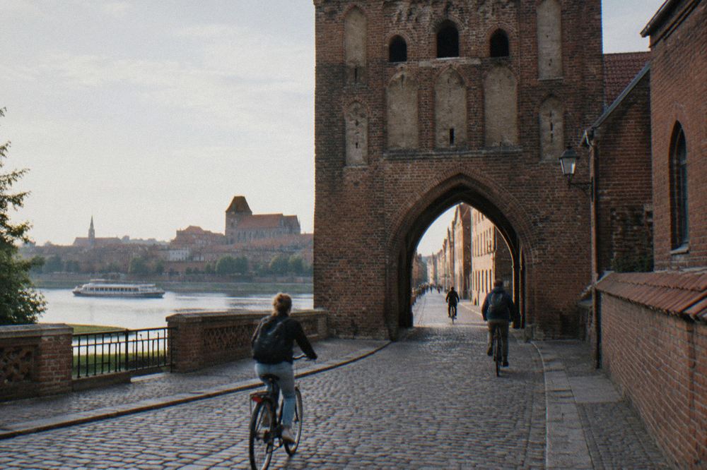 Gothic brick gate tower opening onto a cobbled street with cyclists passing through