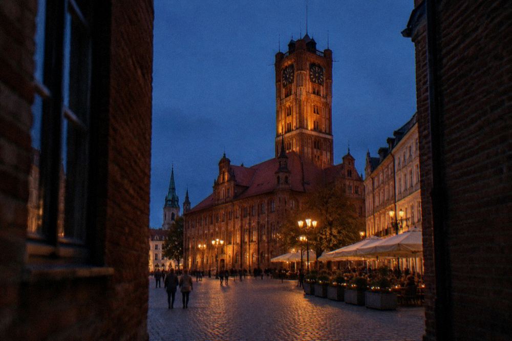 Market square at dusk with the lit town hall tower and outdoor cafe tables along the facades