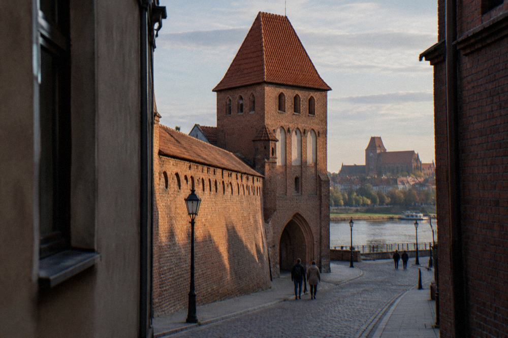 Section of red brick medieval town wall with a gate tower beside a quiet street