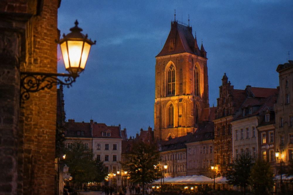 Evening view of a illuminated Gothic church tower above narrow old town rooftops