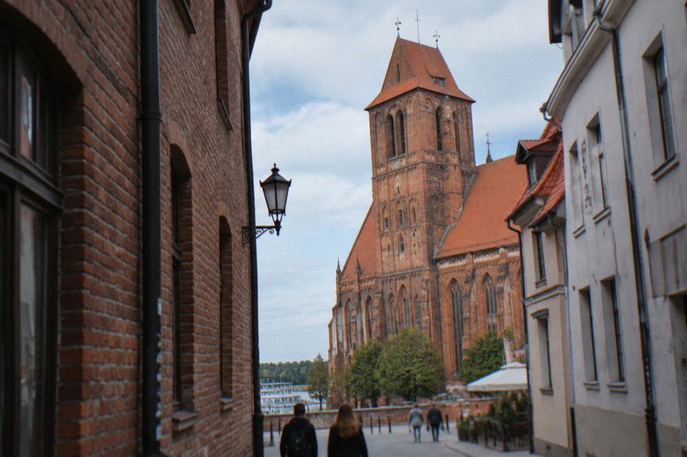 Red brick Gothic cathedral with a tall tower seen from a narrow Old Town street