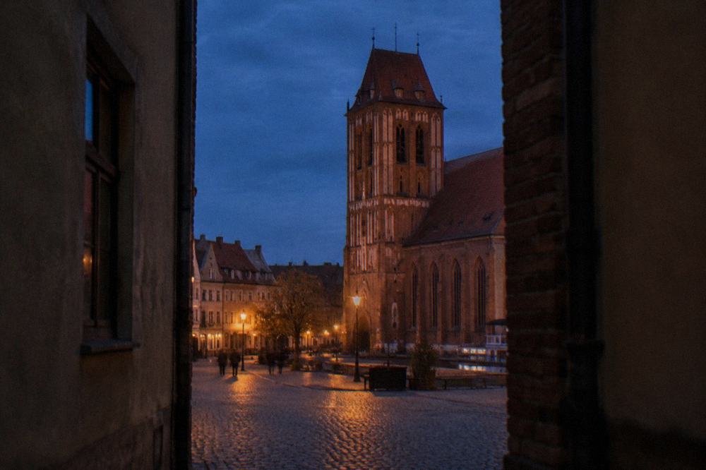 Medieval brick church tower seen from a cobbled square at dusk