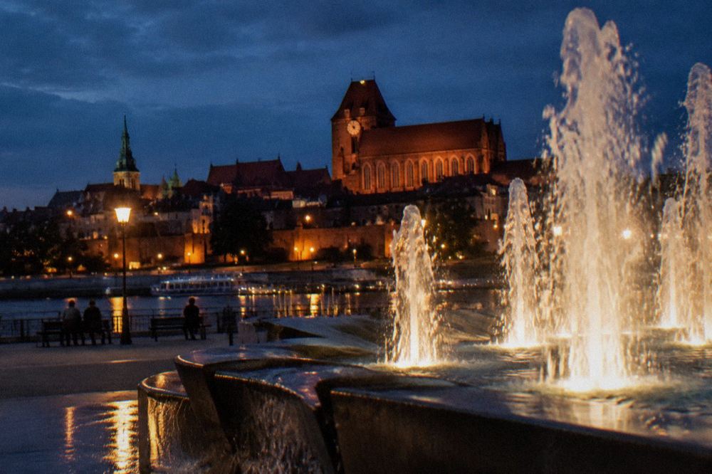Illuminated water jets from a fountain seen against a dark evening sky