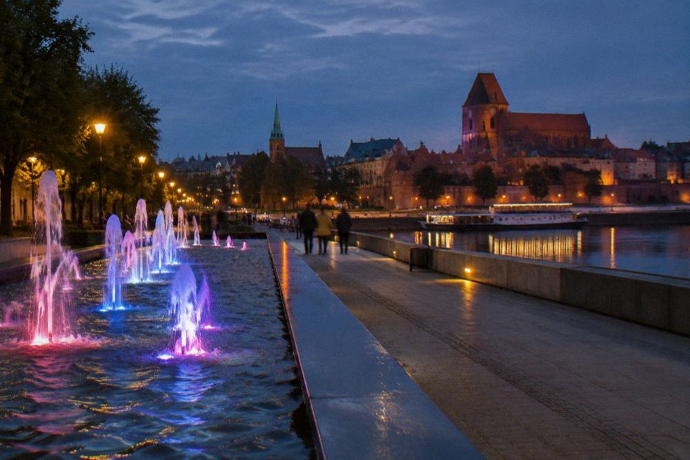 A fountain pool lit with coloured lights beside a walkway in the evening