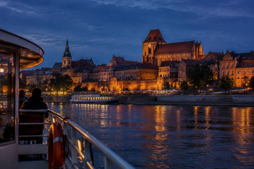 A river cruise boat on the Vistula near the illuminated Old Town of Toruń at night
