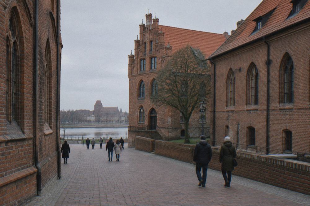 Visitors walking along a brick-paved lane between Gothic buildings in Toruń