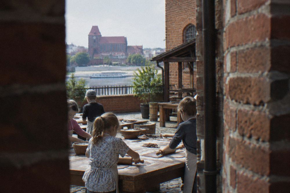 Children rolling gingerbread dough on a floured wooden table during a museum baking workshop
