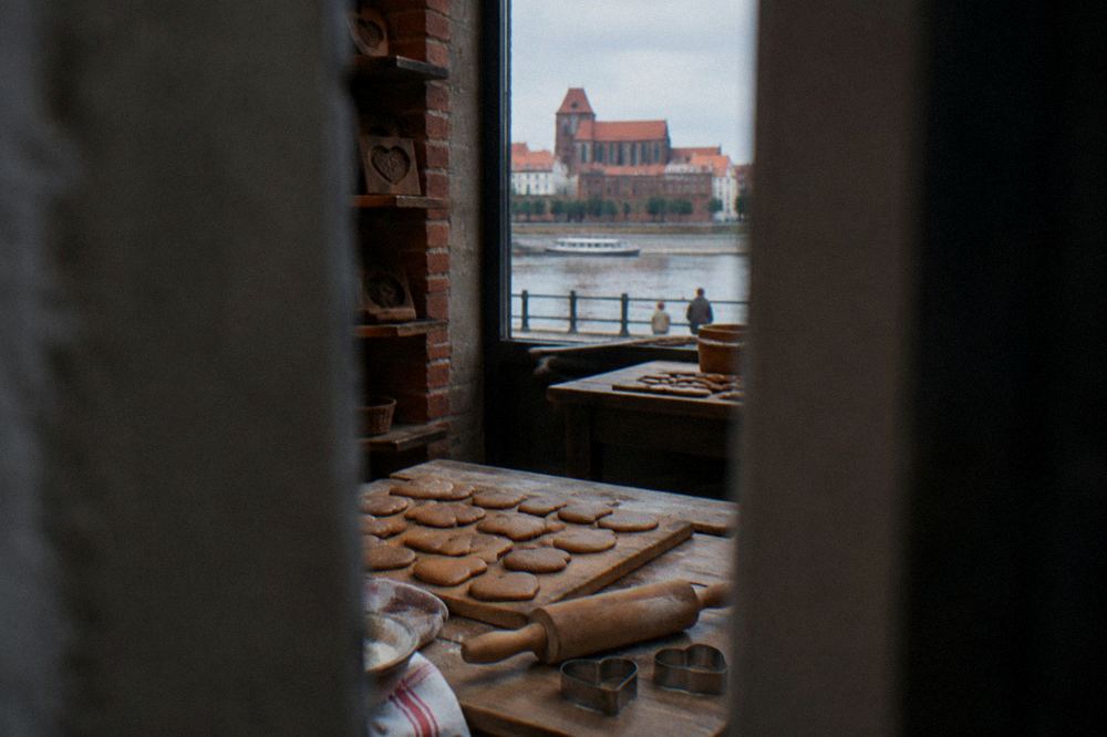A wooden board of round and heart-shaped gingerbread cookies without any writing, a rolling pin and cutters beside, a Toruń bakery table.