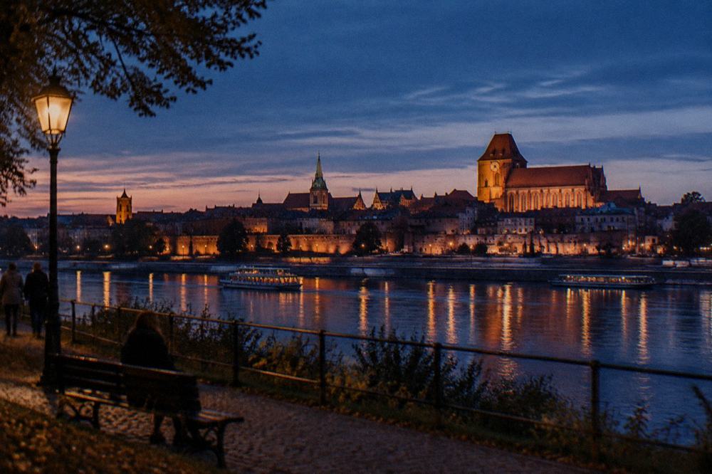 The illuminated Old Town skyline across the Vistula river at dusk in Toruń