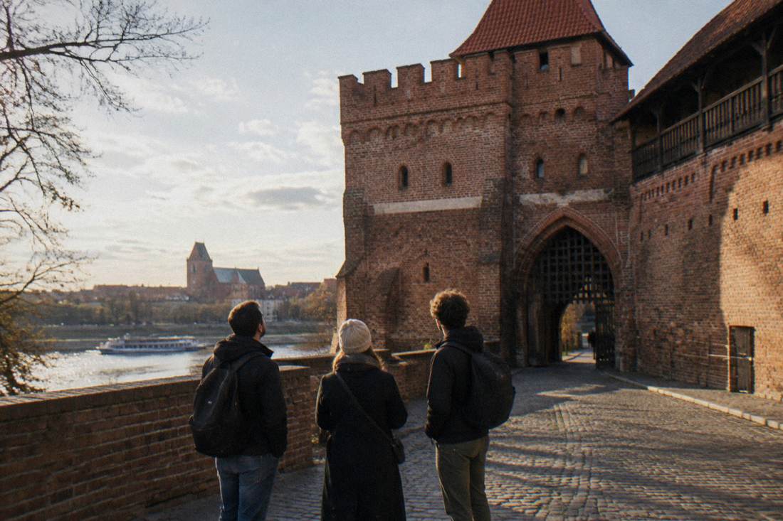 Three people standing by the old town wall and gates in Toruń