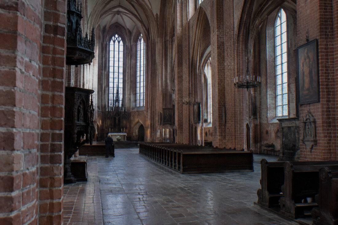 The quiet brick interior of a Gothic church in Toruń with tall arches