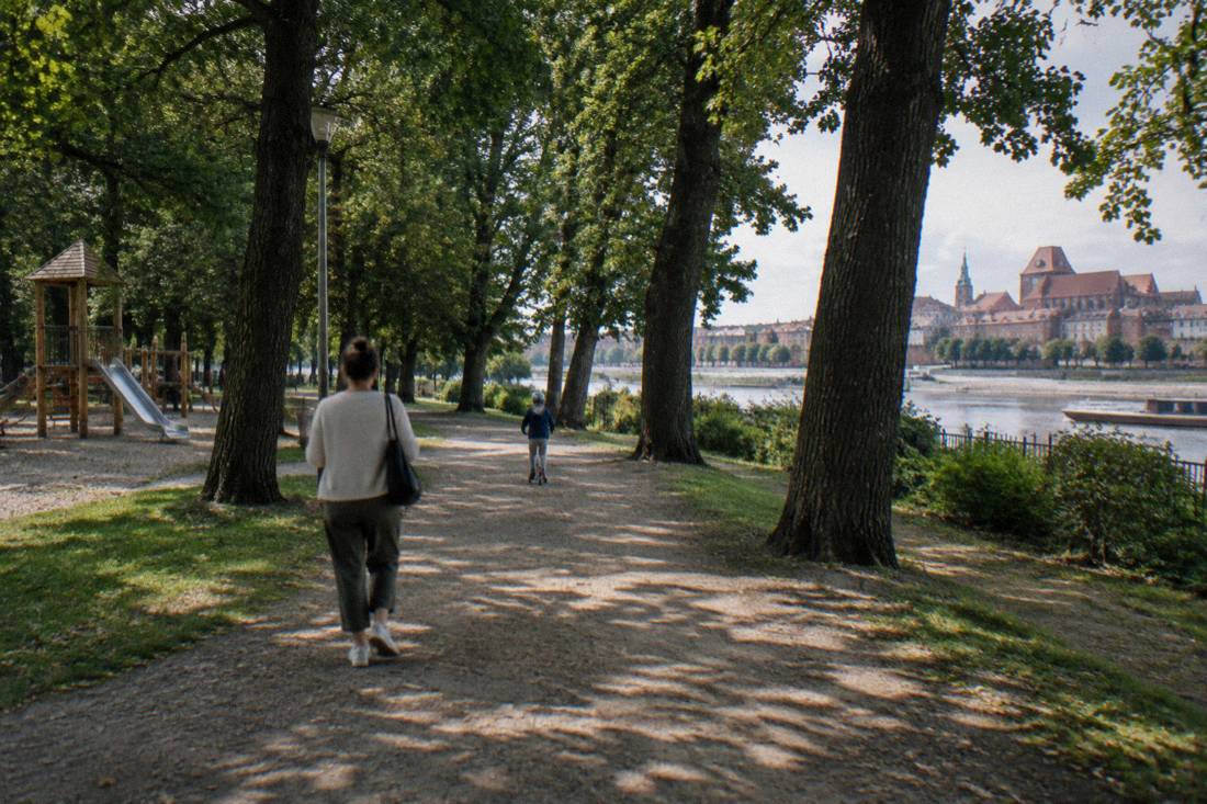 A park path in Toruń with a child on a scooter ahead of a parent