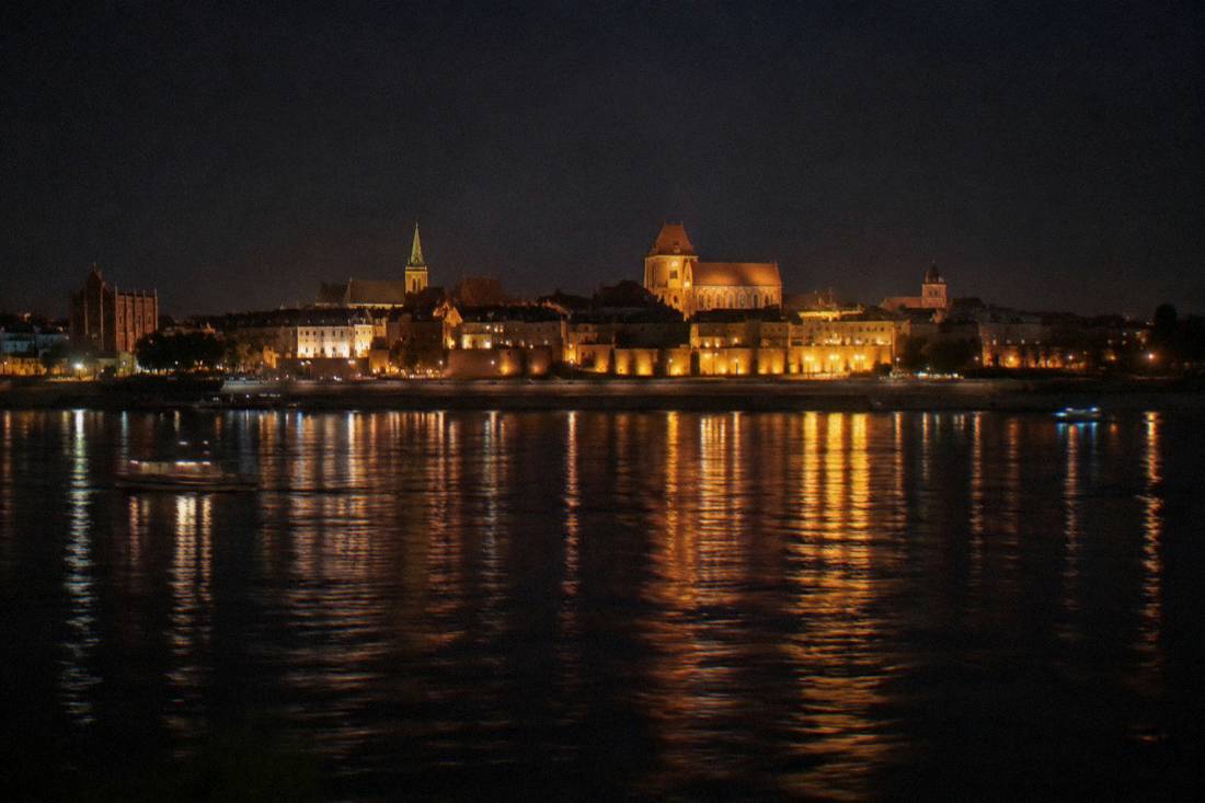 The Toruń waterfront and church roofs reflected in the dark Vistula at night