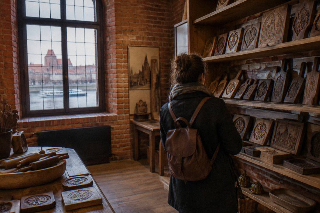 Wooden shelves of baking moulds inside a brick-walled museum room in Toruń