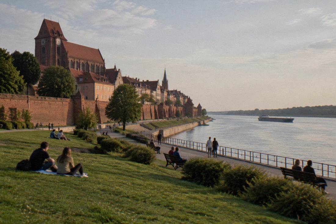 People on the grass and benches along the Vistula embankment below the Toruń town walls