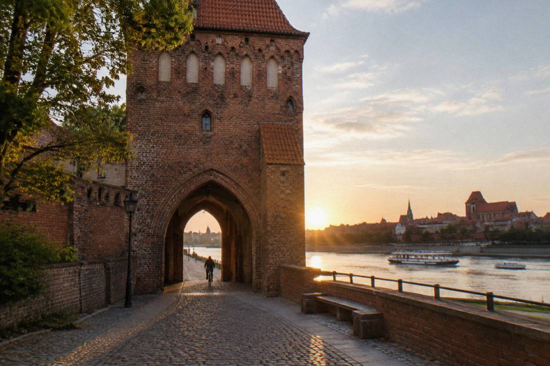 A red-brick fortified town gate in Toruń with an arch onto the riverside path