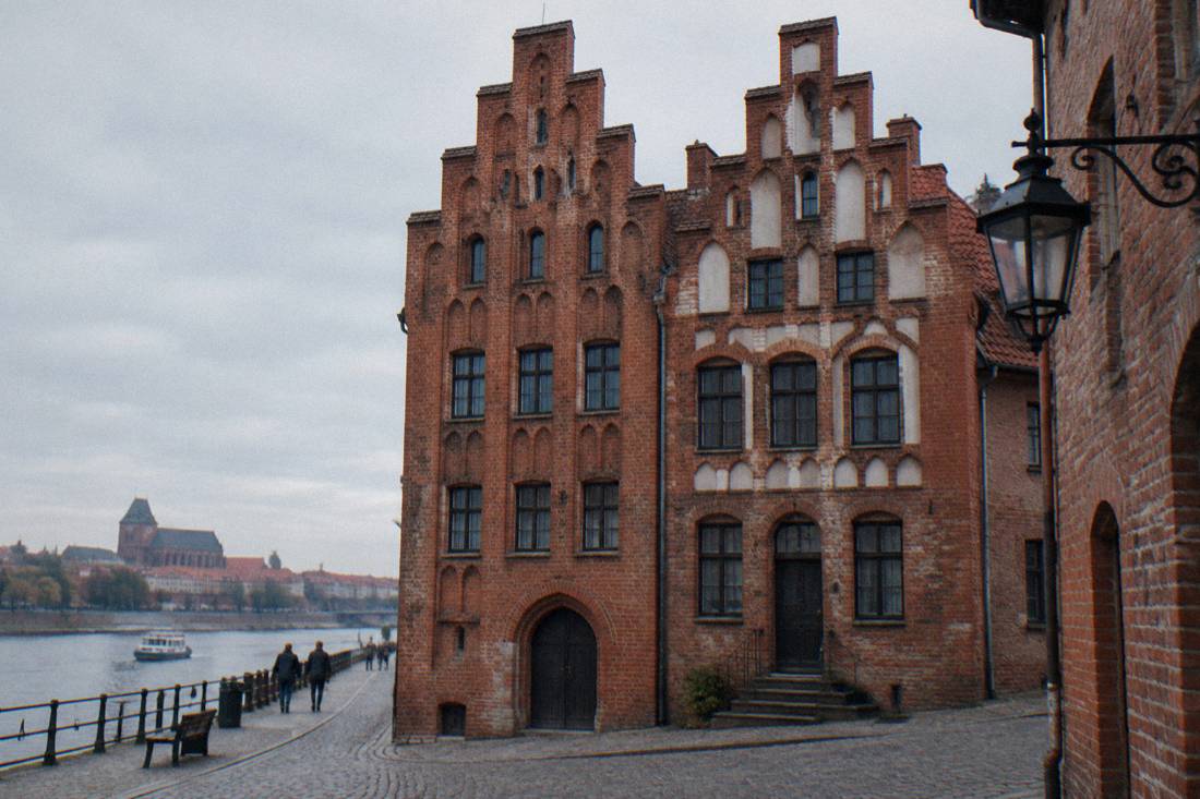 Two narrow Gothic brick townhouses with stepped gables on a Toruń Old Town street
