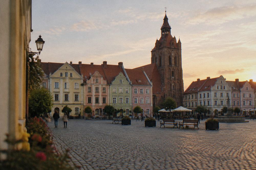 A cobbled market square with pastel-coloured merchant houses and a gothic tower rising behind them