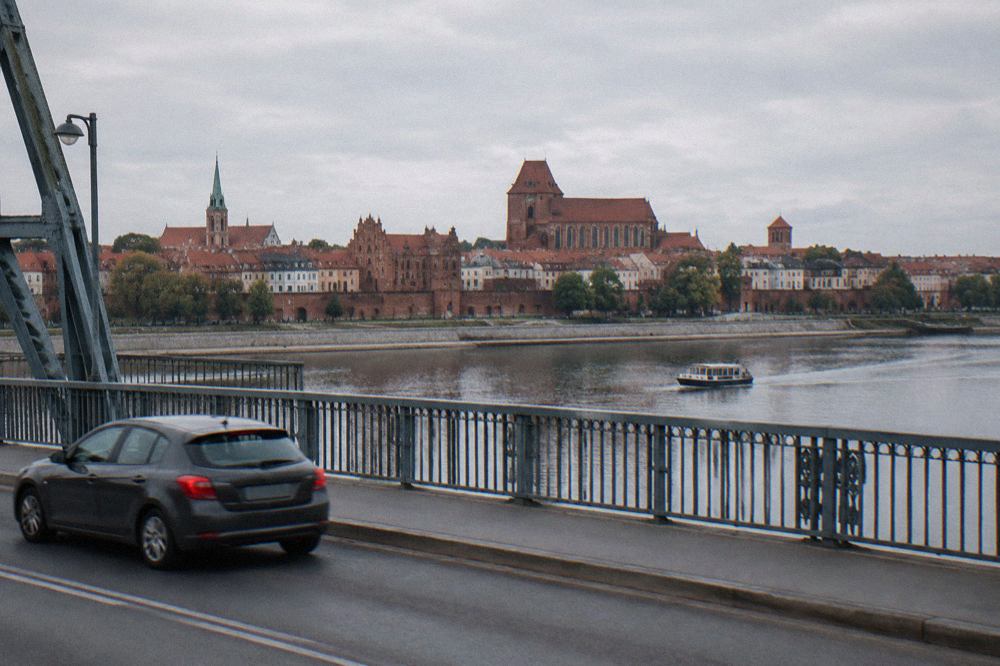 A car crossing a bridge over the Vistula river with a historic town skyline in the background