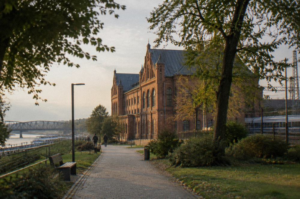 A red-brick industrial museum building surrounded by trees seen from a path
