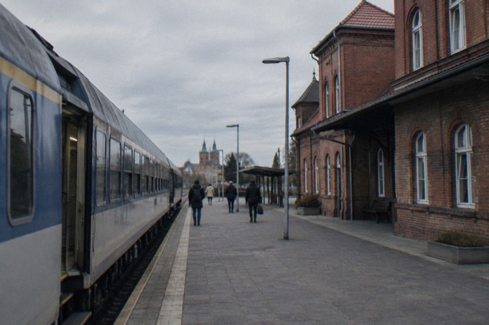 A passenger train standing at a platform beside a Polish station building