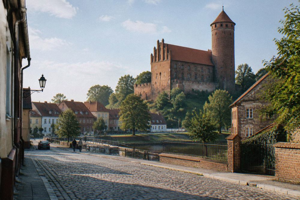 A brick Gothic castle with a tall round tower rising above a small Polish town