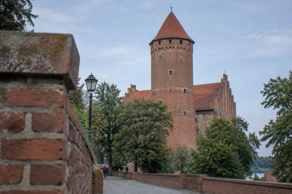 A red-brick castle tower against a blue sky with trees at its base
