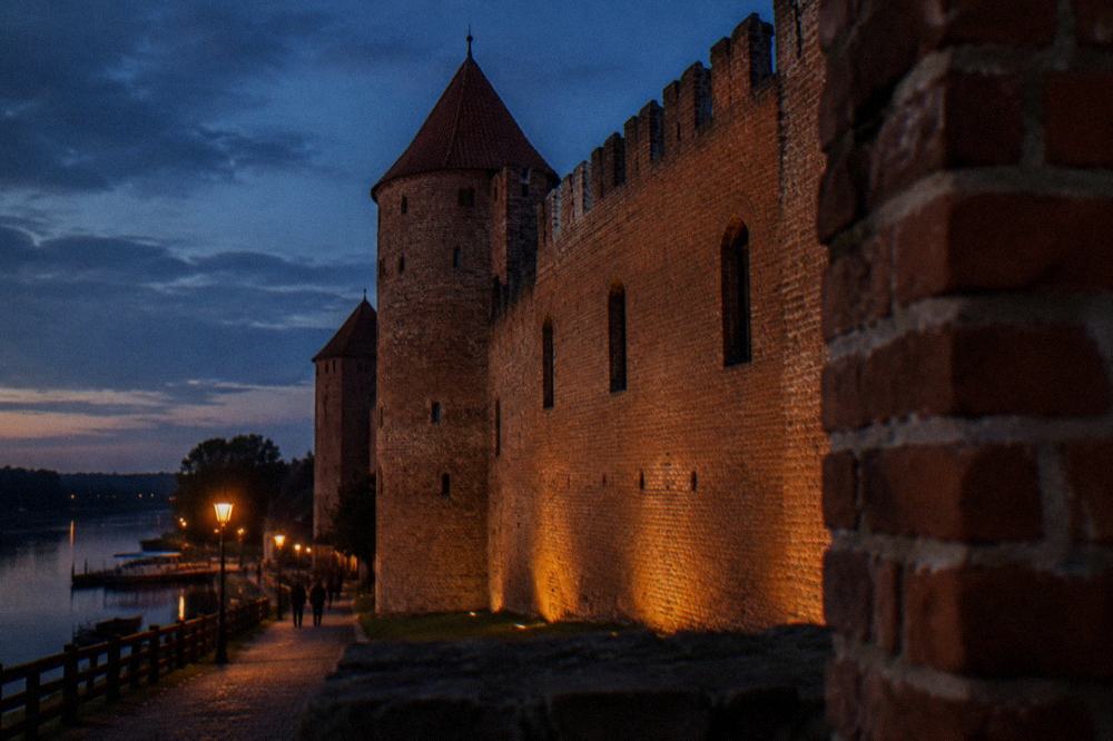 Evening light on a brick castle wall with narrow windows and crenellations
