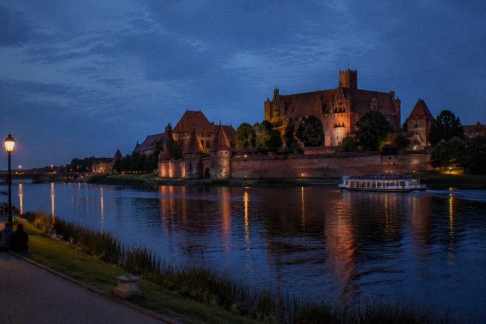 Wide view of Malbork Castle from across the river at dusk