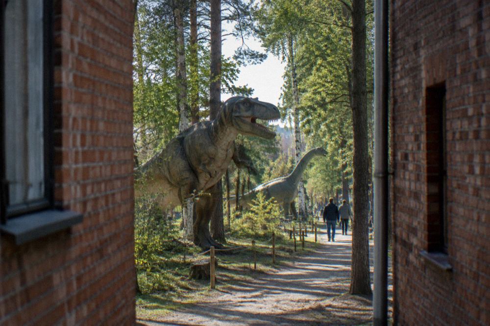 Life-size dinosaur models standing among trees along an outdoor trail at a dinosaur park