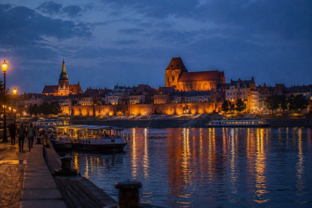 Illuminated historic buildings along the Vistula riverfront in Toruń at night
