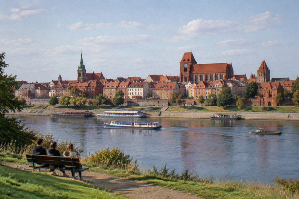 Panoramic view across the Vistula River to the red brick roofs and church towers of the Toruń Old Town on a bright day