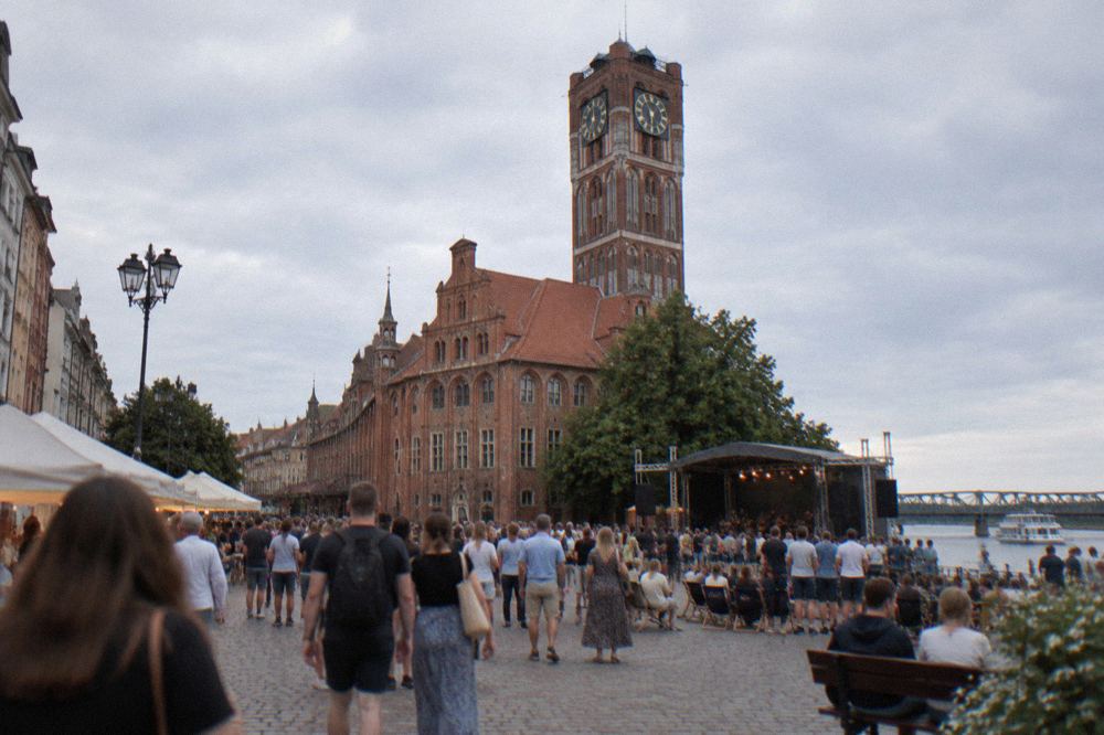 Crowd at an open air summer event on a Toruń market square with gothic town hall tower in the background