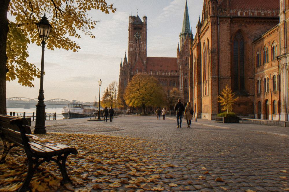 Autumn leaves on a cobblestone street in Toruń with brick gothic facades in golden late afternoon light