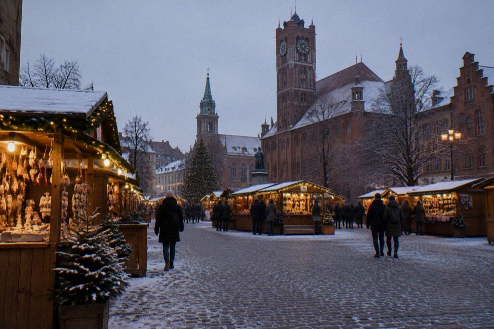 Festive wooden market stalls with lights on the Toruń Old Town square at dusk in winter