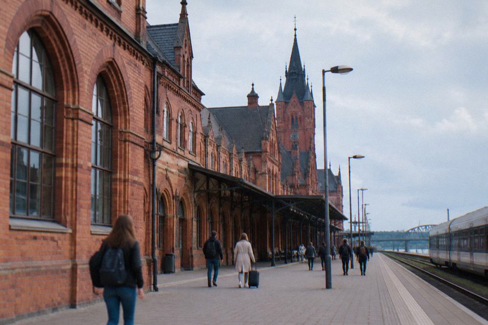 Red brick railway station building with passengers walking along the platform