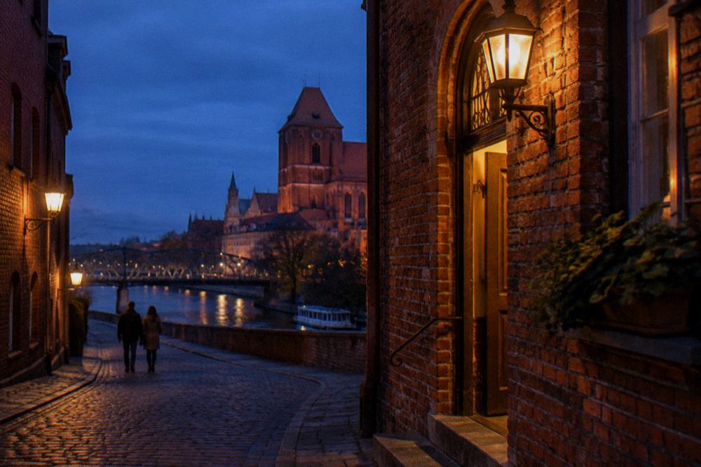 A narrow Old Town lane in Toruń after dark, warm lamps on brick walls and a lit doorway glowing, a couple walking away.
