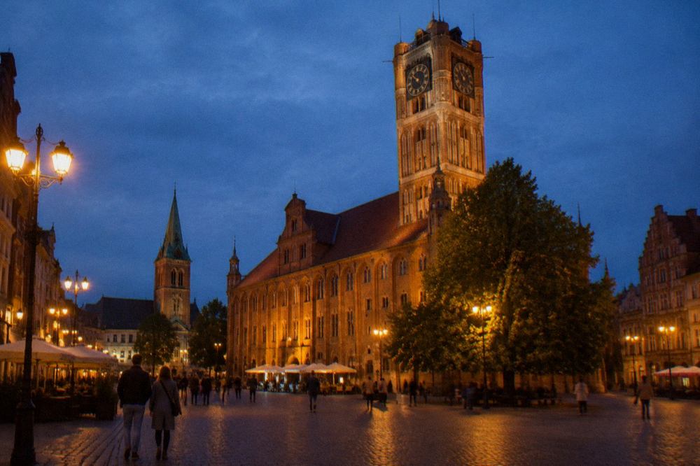 Evening view of Toruń Old Town market square with illuminated town hall and gothic facades