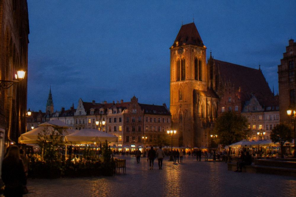 Illuminated gothic church tower and old town houses at dusk in Toruń