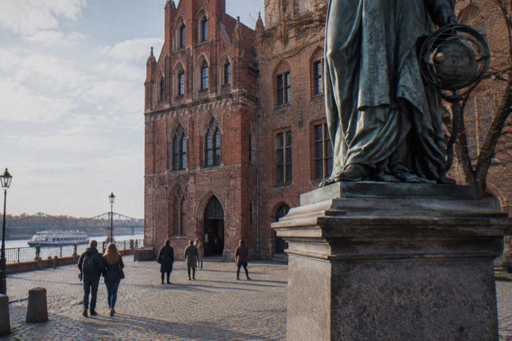 Visitors on a cobbled street outside a Gothic brick museum building in Toruń