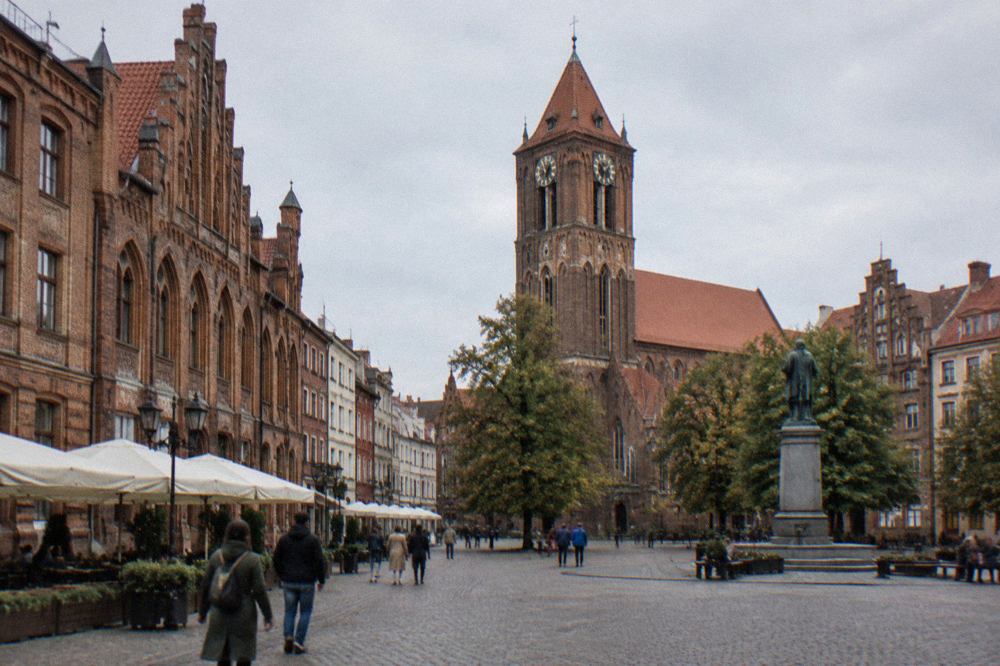 Red-brick Gothic townhouses and a church tower above the old square of Toruń in daylight