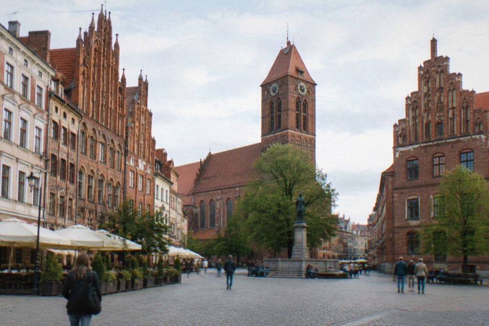 Red brick Gothic townhouses and a church tower above the Old Town square of Toruń on a bright day